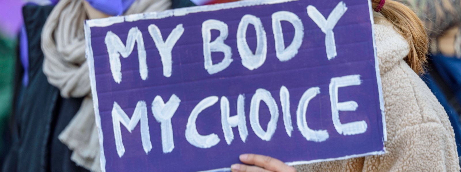 Frau, die ein lila Schild hält, auf dem steht: My Body, My Choice