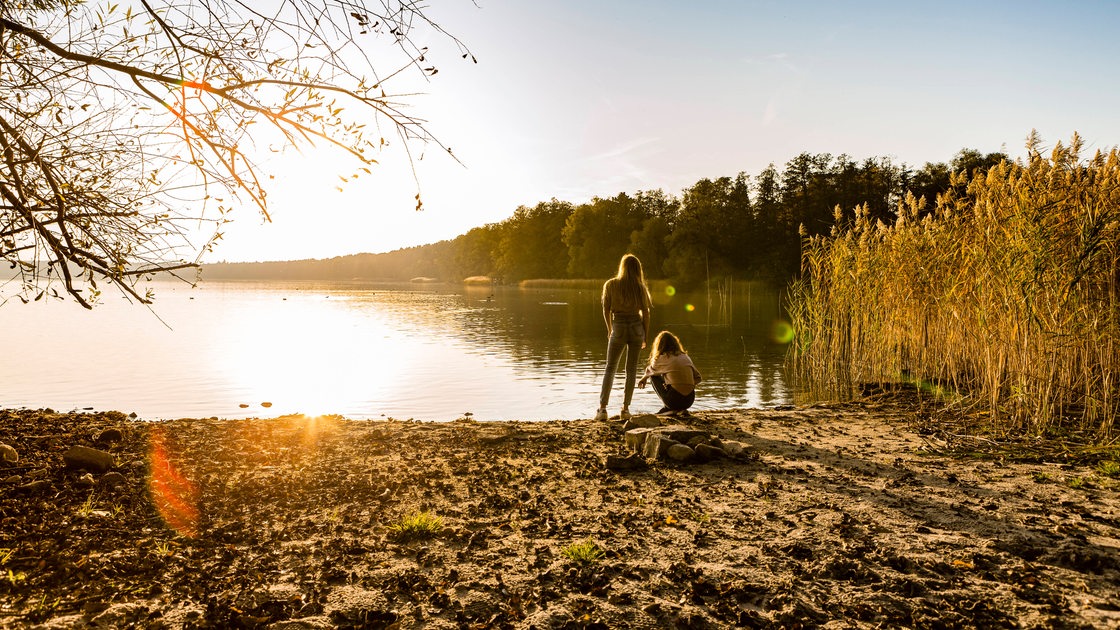 Zwei Mädchen stehen bei Sonnenuntergang an einem See