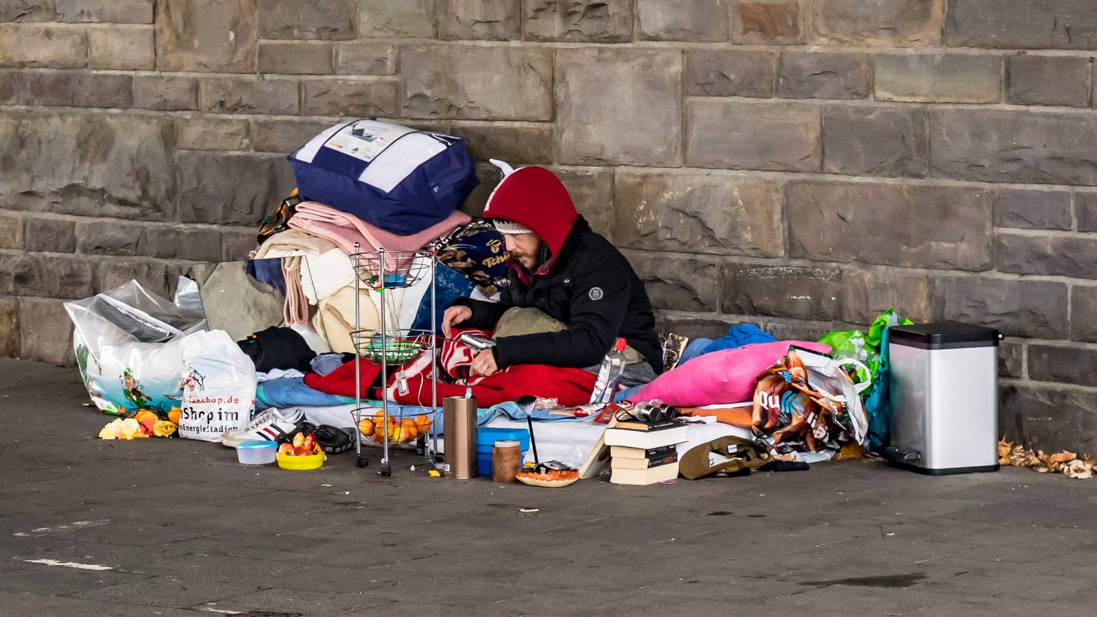 Ein obdachloser Mann sitzt mit seinen Habseligkeiten an einer Steinmauer (Archivbild)