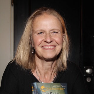 Autorin Cornelia Funke hält ihr Buch im Arm und lächelt