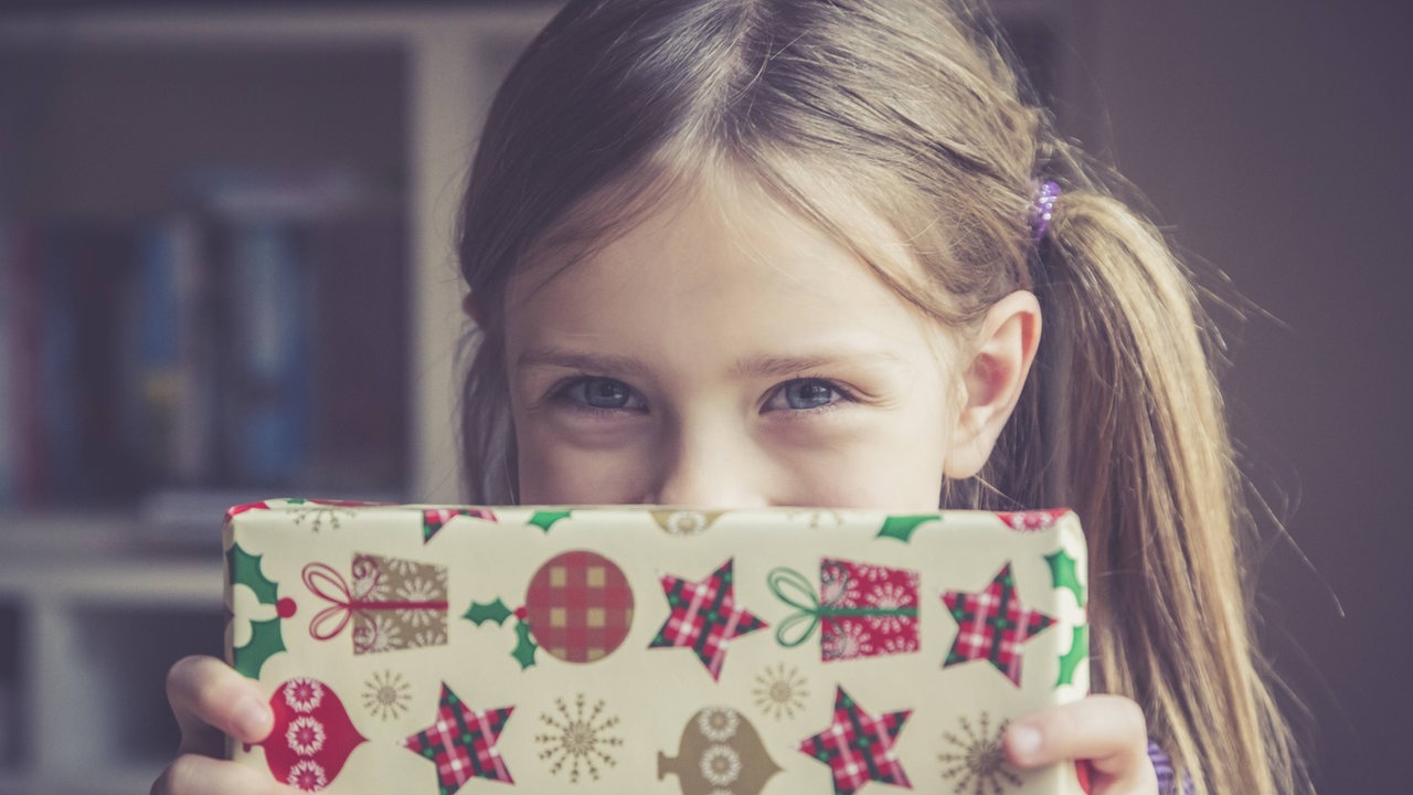 Ein Mädchen hält ein Geschenk vor ihrem Gesicht