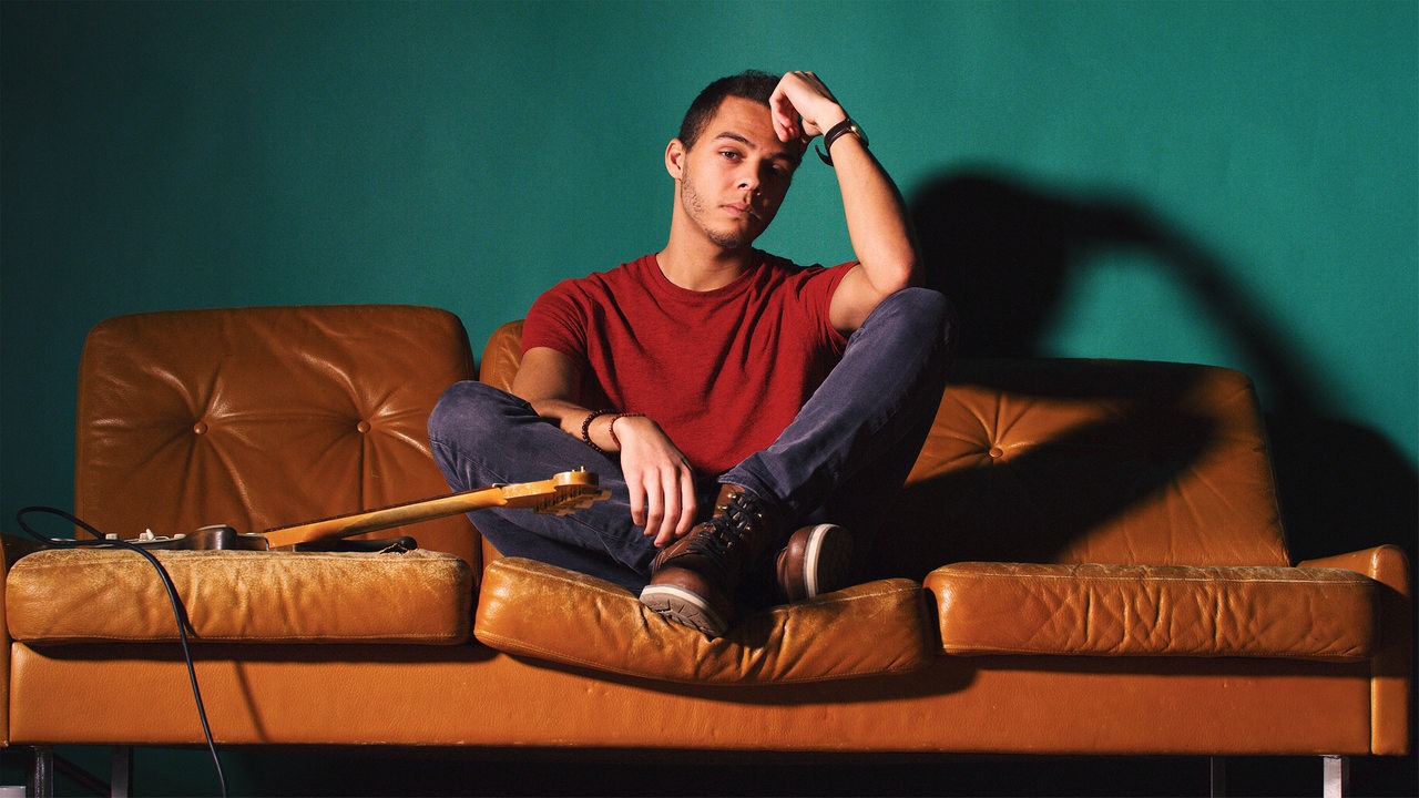 Sänger Malik Harris vor grüner Wand auf braunem Sofa