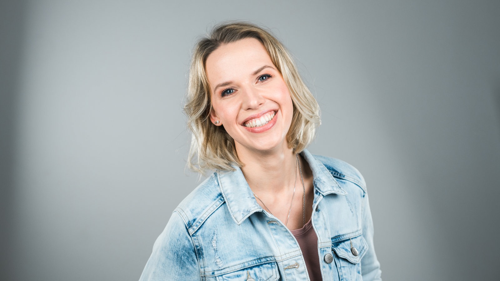 Morgenshow-Teammitglied Marilena Dahlmann in einer blauen Jeansjacke lächelt in die Kamera
