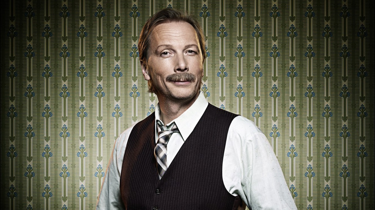 Comedian Pawel Popolski vor grüner gemusterter Tapete 