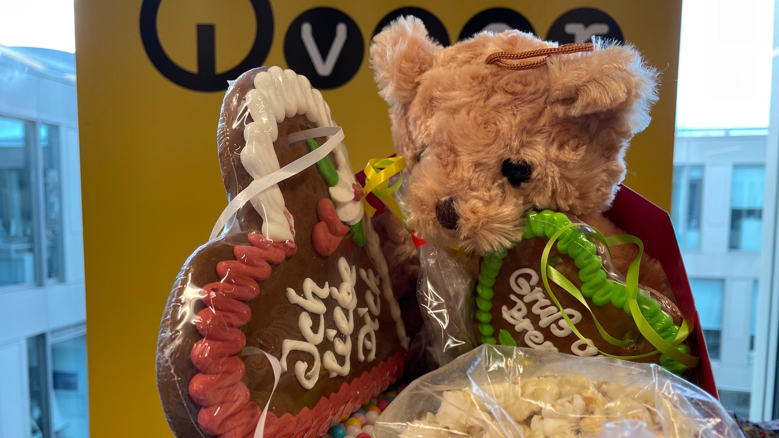 Bunte Lebkuchenherzen, Popcorn und ein hellbrauner Teddybär vor einem gelben Bremen-Vier-Logo.