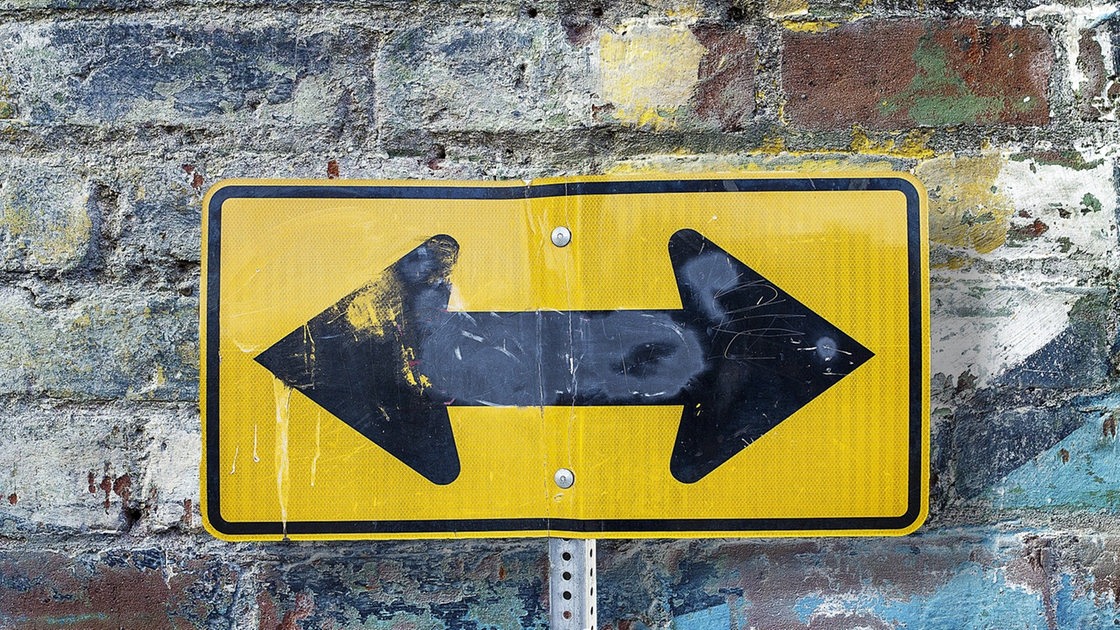 Ein gelbes Schild mit zwei entgegengesetzten Pfeilen