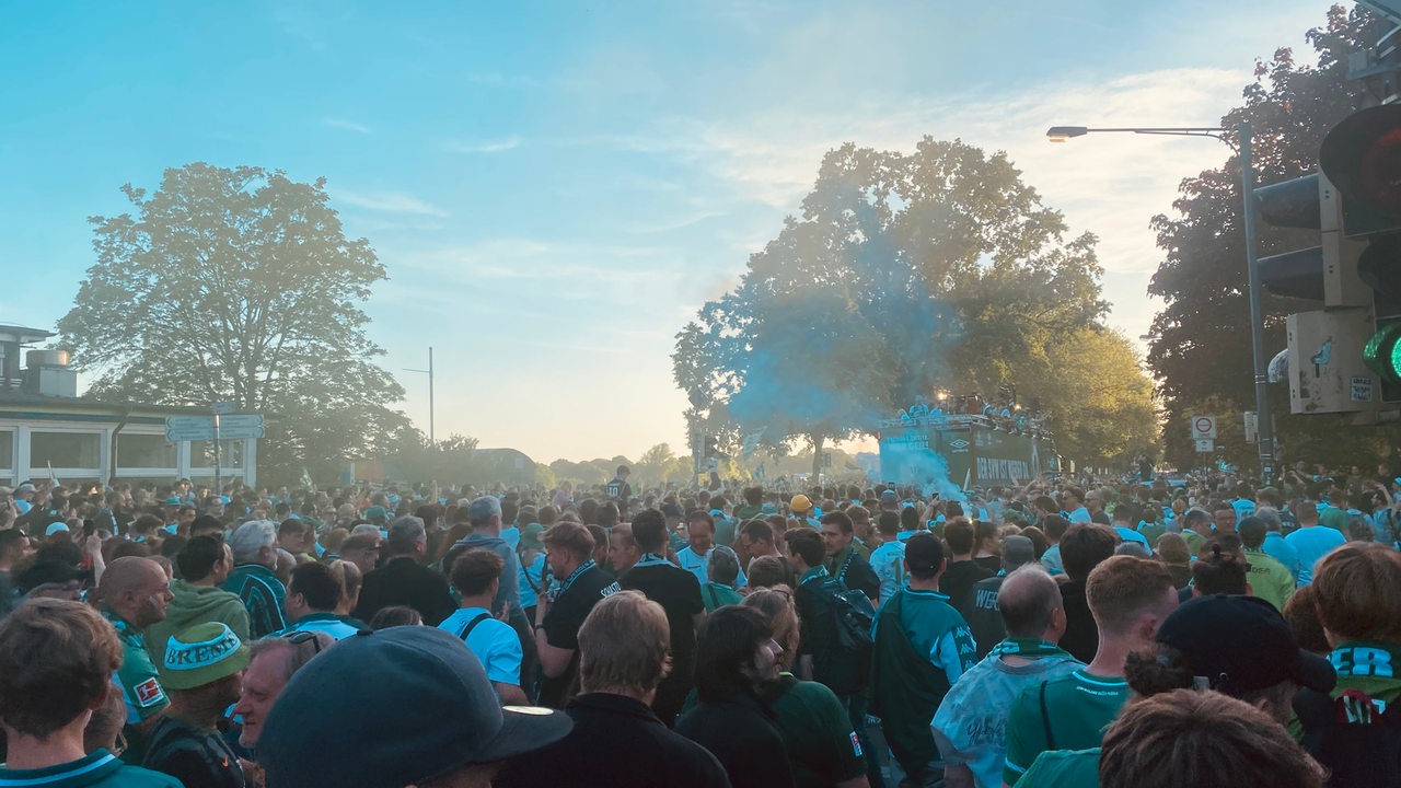 Werderfans jubeln am Osterdeich, im Hintergrund sieht man den Bis mit Werderspielern.